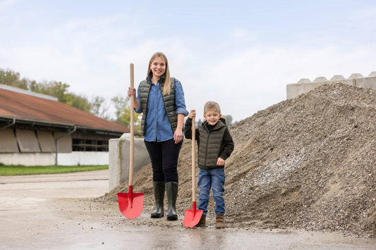 Frankfurter Schaufel mit Stiel Mini für Kinder, ideal für Gartenarbeiten, neben Erwachsenenschaufel vor Kieshaufen präsentiert.