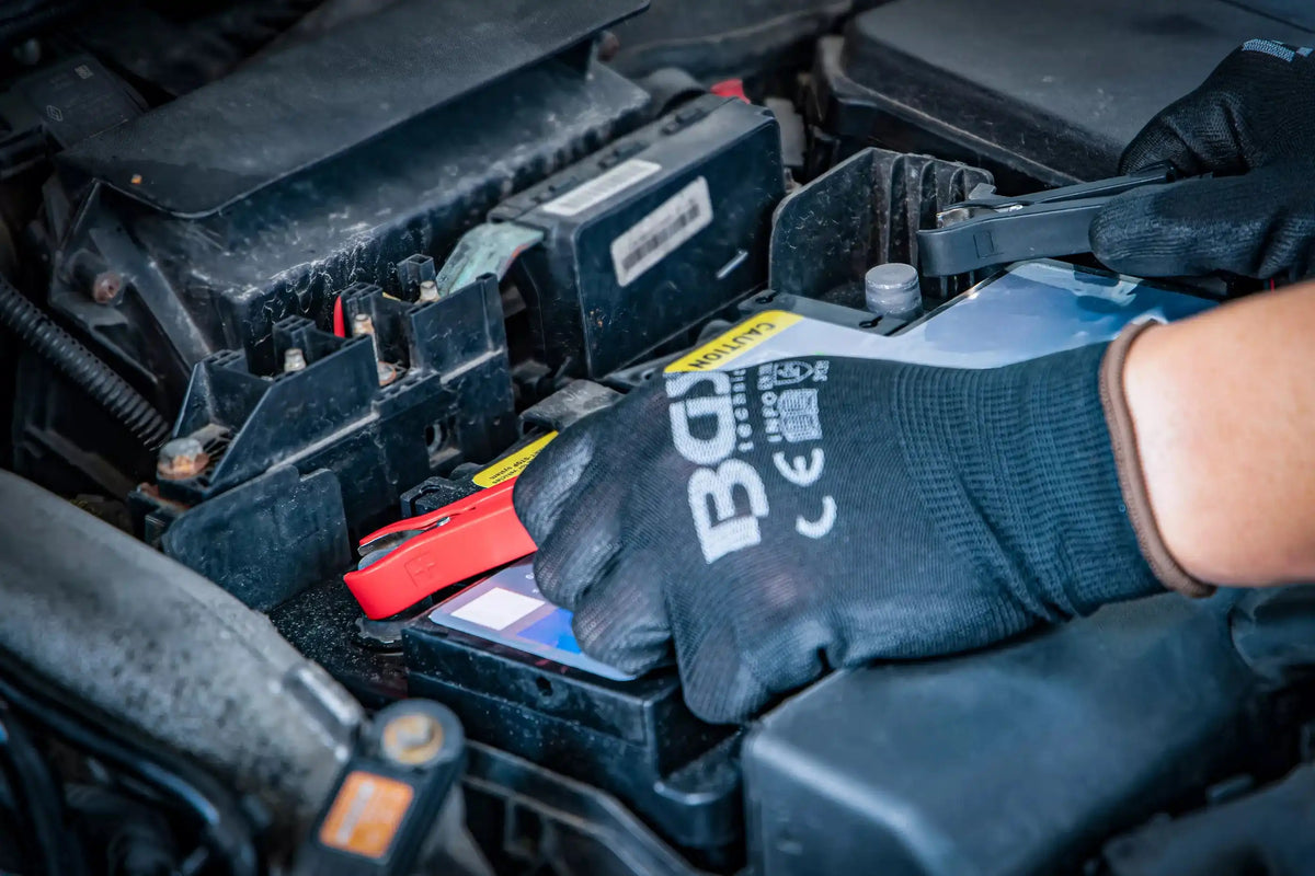 Anschluss des digitalen Batterie-Ladegeräts 6/12 V an eine Autobatterie durch eine Person mit BGS-Handschuhen für sichere Handhabung.